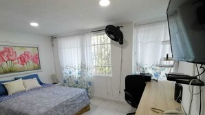 Een slaapkamer met een bed, een bureau met een computer, een stoel en een televisie.