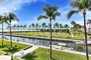 A canal with boats, palm trees, and a grassy area with a pathway.