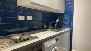 A compact kitchen with a stove, sink, and built-in washing machine. - Three Bed Two Bath Apartment in London (London)