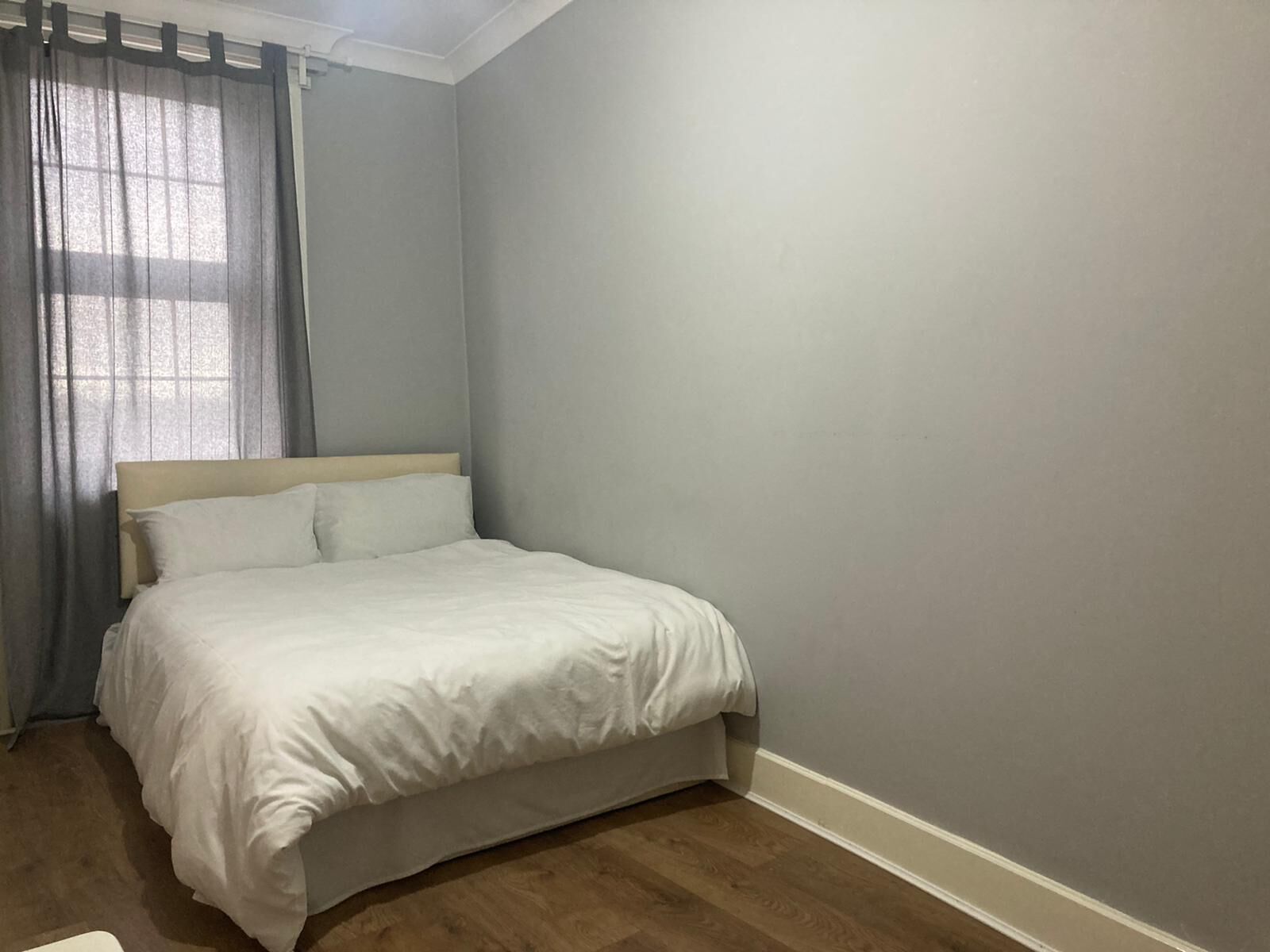 Quarto com cama, janela com cortinas e parede lisa.