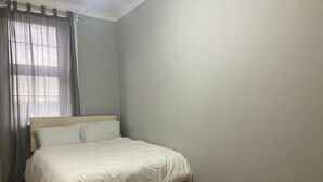 A bedroom with a bed, a window with curtains, and a plain wall. - Three Bed Two Bath Apartment in London (London)