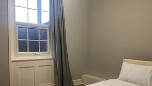 A bedroom with a single bed, a window with curtains, and a white headboard. - Three Bed Two Bath Apartment in London (London)