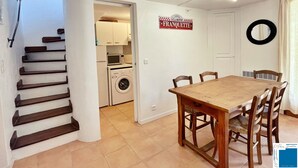 A compact kitchen with a washing machine, a dining area with a wooden table and chairs, and a staircase leading to another room.