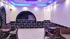 Restaurante com parede de tijolos e janela circular. Mesas e cadeiras dispostas para refeições.