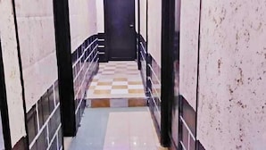 Um corredor com piso xadrez, uma porta preta no final e teto com iluminação azul.