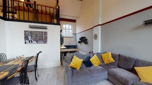 A modern living space with a grey sofa, wooden dining table, and a staircase leading to an upper level.