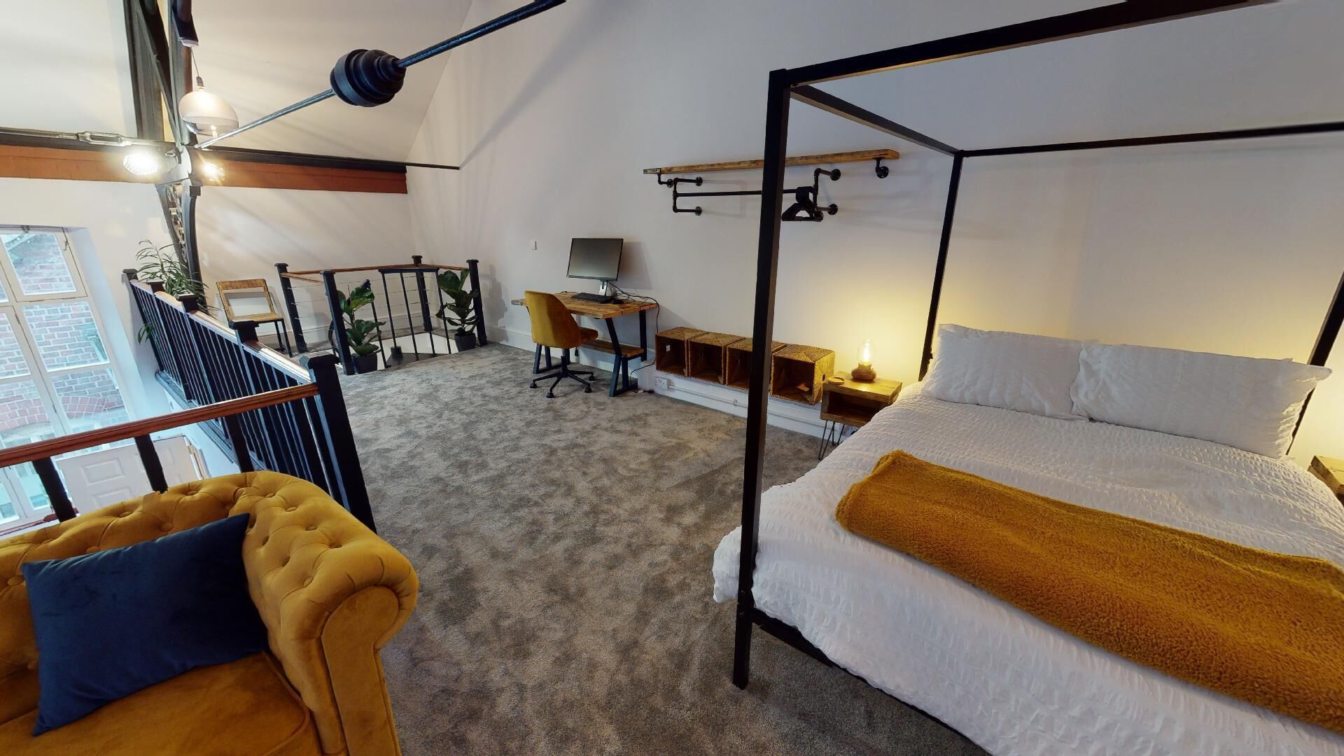 A room with a four-poster bed, a desk with a computer, a chair, and a staircase leading to an outdoor area with plants.
