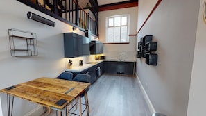 A compact kitchen with a wooden dining table, dark cabinetry, and a window providing natural light. - Hu1 Boutique City Apartment - Sleeps 6 (Hull)