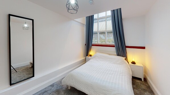 Un dormitorio con cama, mesitas de noche, un espejo y una ventana con cortinas.