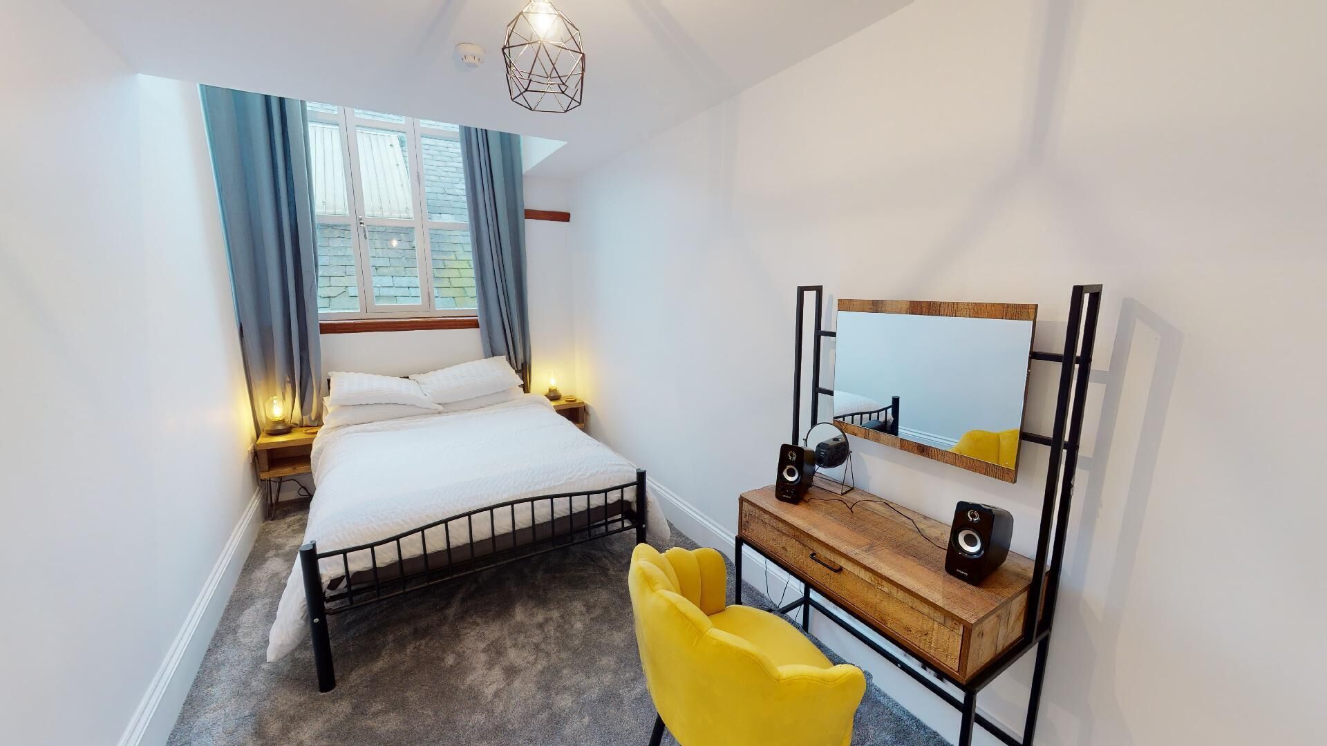 A bedroom with a bed, bedside table, lamp, mirror, and a yellow chair.