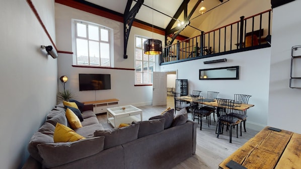 A modern living room with a grey sofa, wooden dining table, and a staircase leading to an upper level.