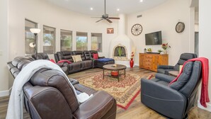 Ein geräumiges Wohnzimmer mit Ledersofas, Kamin, Flachbildfernseher und Deckenventilator.