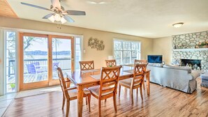 A spacious living room with a wooden dining table, comfortable seating, a fireplace, and a balcony with a view. - Sunny Lakefront Family Paradise w/ Deck & 2 Kayaks (Granbury)