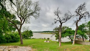 A grassy area with a stone wall, trees, and a view of a lake. - Sunny Lakefront Family Paradise w/ Deck & 2 Kayaks (Granbury)