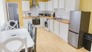Una cocina compacta con armarios blancos, un refrigerador de acero inoxidable, un microondas y una lavadora.