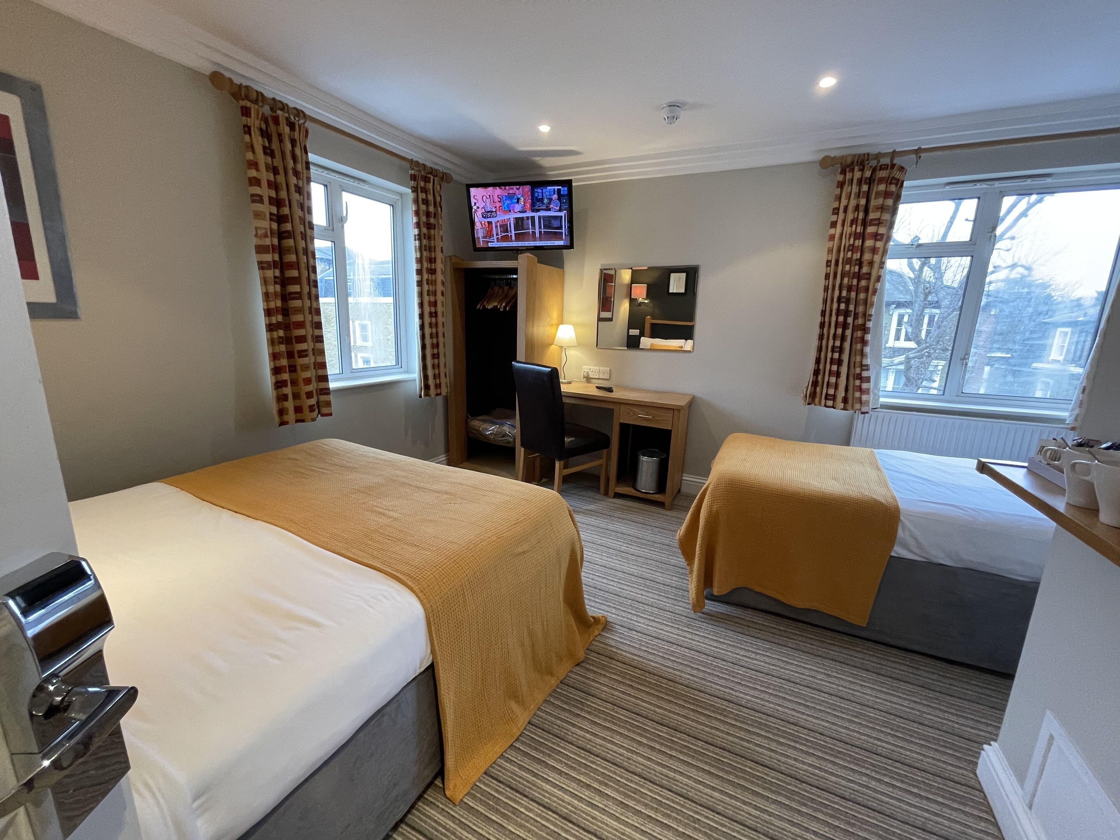 A hotel room with two beds, a desk, a television, and a window with curtains.