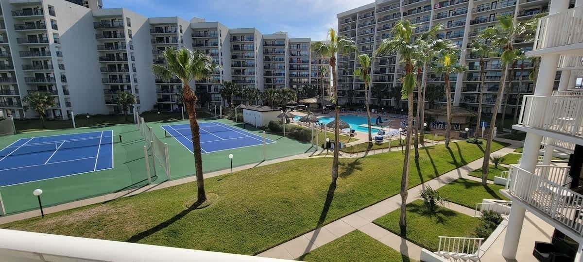 A view of a hotel with multiple floors, a tennis court, and a pool area.