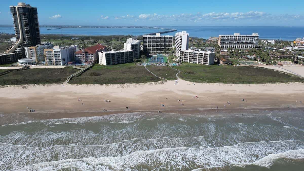 Zona hotelera costera con propiedades frente a la playa, una playa de arena y olas del océano.