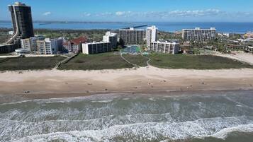 Zona hotelera costera con propiedades frente a la playa, una playa de arena y olas del océano.
