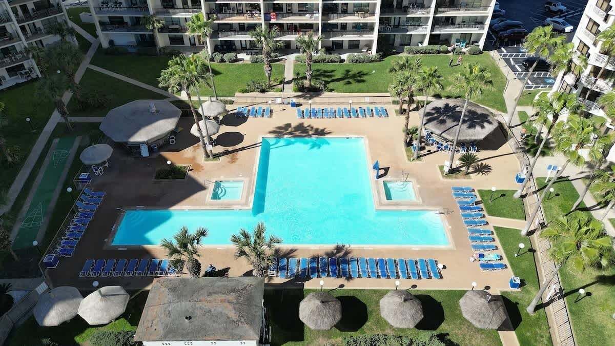 Ein Hotelpoolbereich mit großem zentralen Pool, Liegestühlen und Palmen.