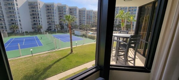 A balcony with a view of a tennis court and apartment buildings.