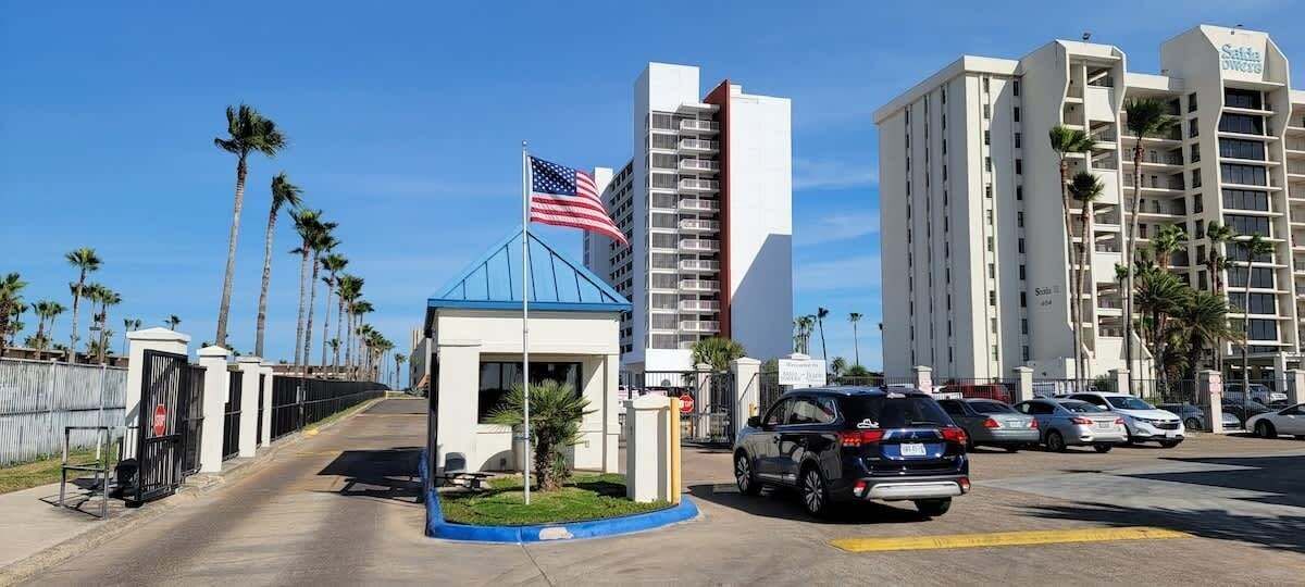 A hotel entrance with a blue roof, an American flag, and a parking lot with cars.