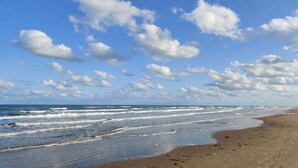 En strand med vågor, en klar himmel och några få moln här och var.