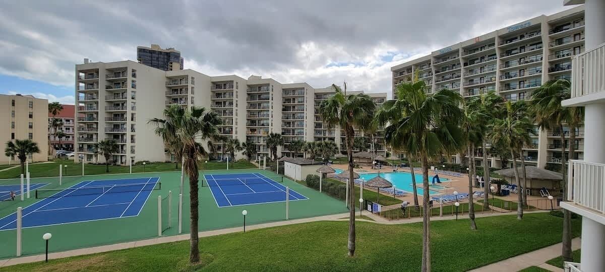 A hotel with multiple tennis courts, a swimming pool, and palm trees.