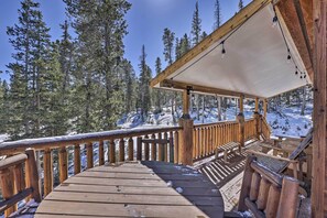 Relax on the deck with a covered seating area and benches, surrounded by the serene beauty of the snowy forest.
