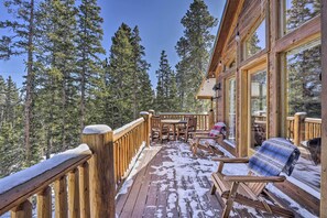 Enjoy the serene forest views from the cabin's spacious deck, featuring a table, chairs, and a cozy rocking chair.