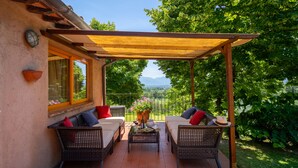 Een terras buiten met rieten meubilair, een pergola en uitzicht op een weelderige tuin en verre bergen.