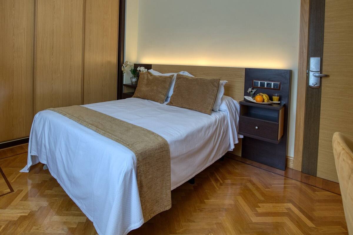 A neatly made bed with a wooden headboard, a bedside table with a fruit bowl, and a wardrobe.