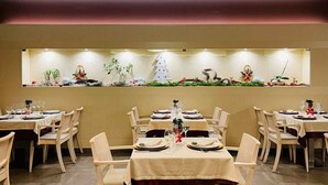 Un restaurante con varias mesas preparadas para comer, cada una con manteles blancos y vajilla y cubertería ordenadas.