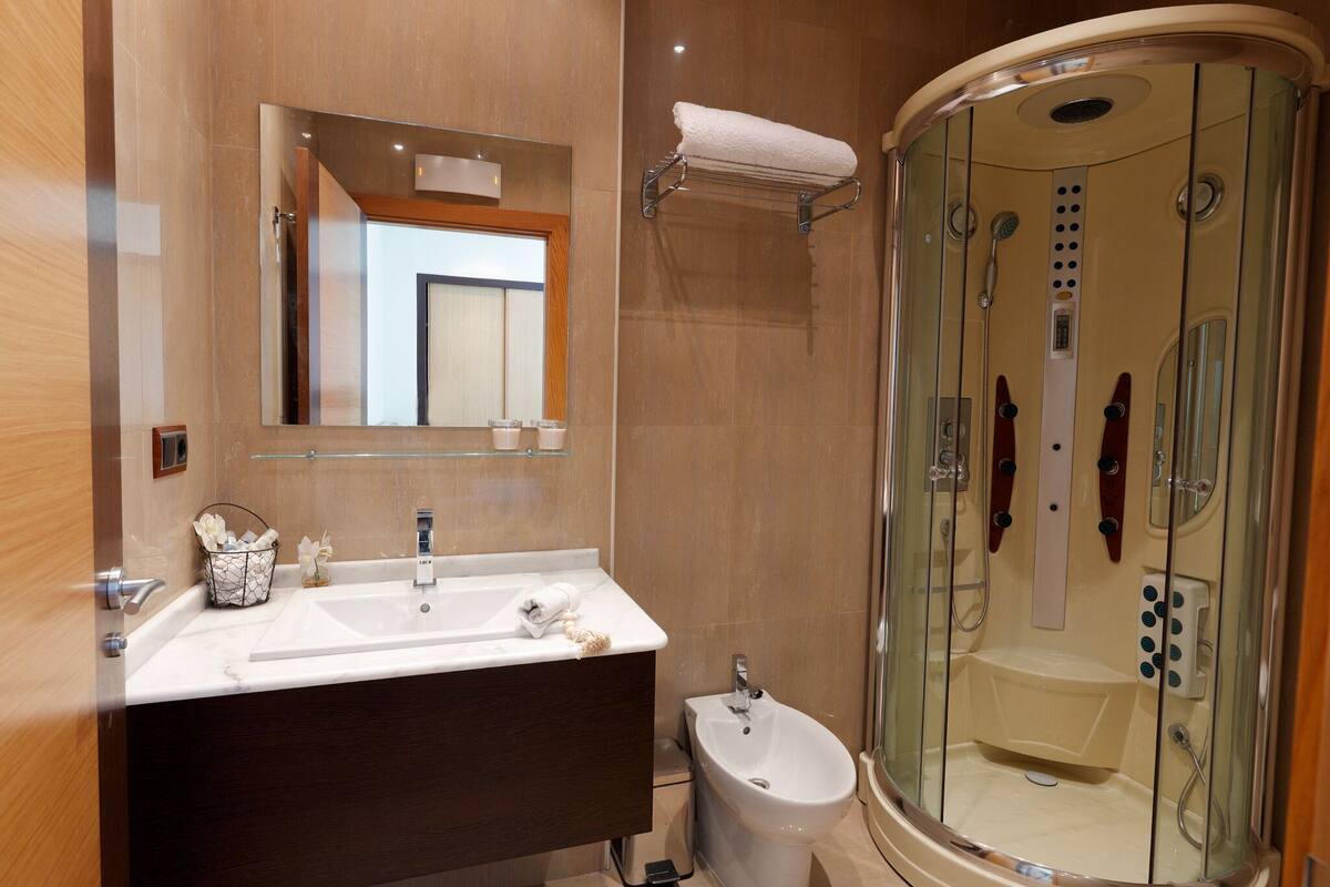 A modern bathroom with a large mirror, a sink, a bidet, and a glass-enclosed shower area.