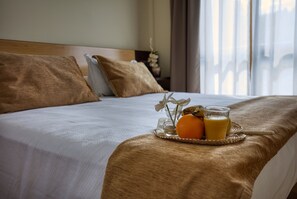 Ein ordentlich bezogenes Bett mit einem Tablett mit Orangensaft, einem Glas Orangensaft, einem Kissen und einem Nachttisch mit Blumen in einer Vase.
