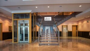 Un moderno vestíbulo de hotel con piso de mármol, un ascensor de vidrio y una escalera con barandillas de metal.