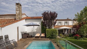 A swimming pool with lounge chairs and an umbrella, surrounded by a wooden deck and a garden.