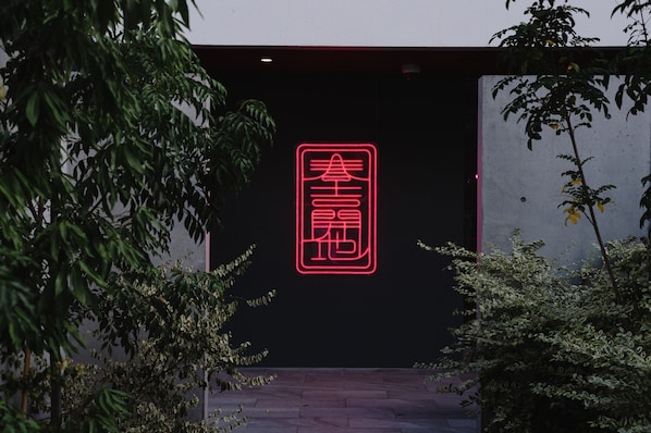 A neon sign with Chinese characters on a dark wall, surrounded by greenery.