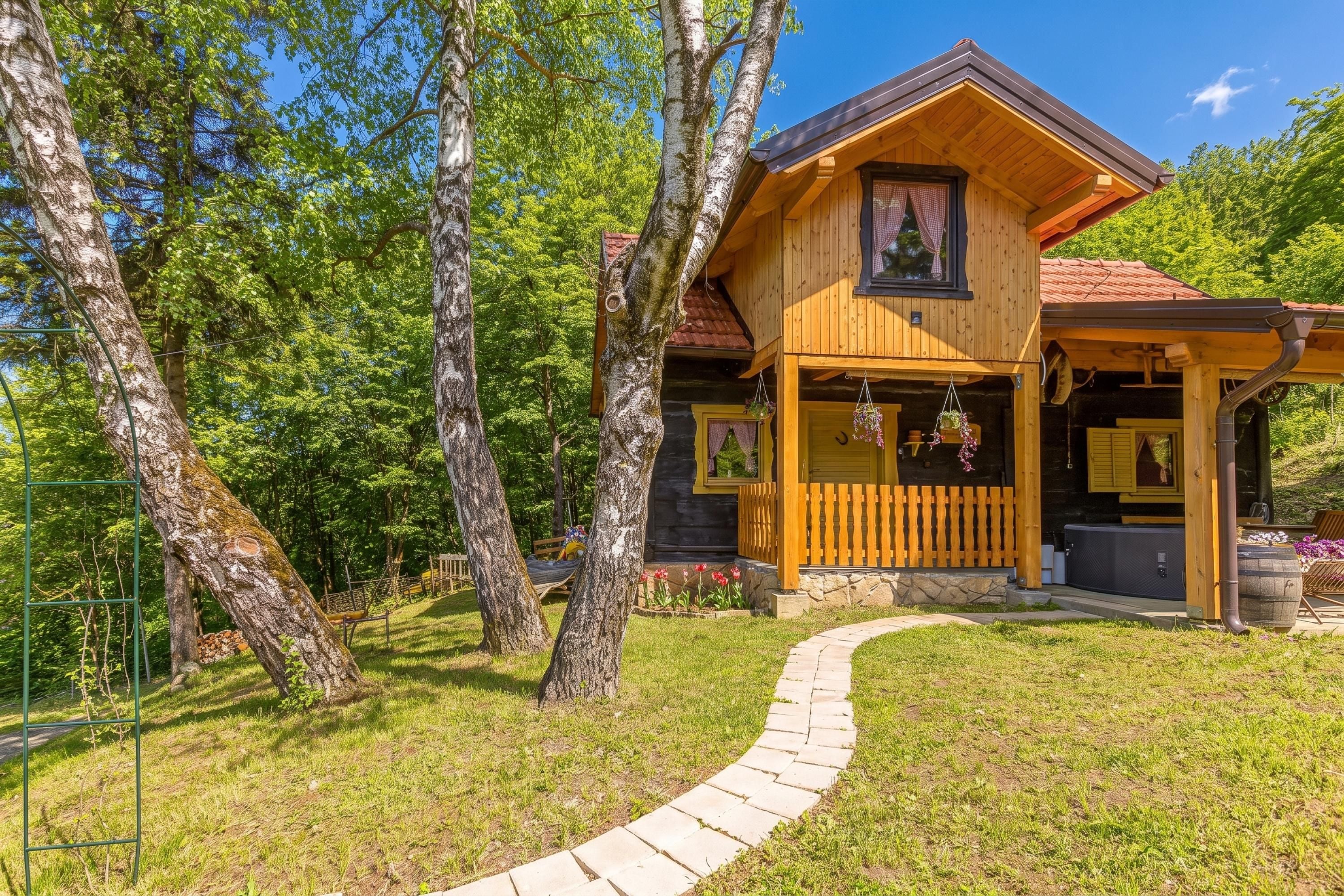 Una baita di legno con un portico, immersa tra alberi e un sentiero in pietra.