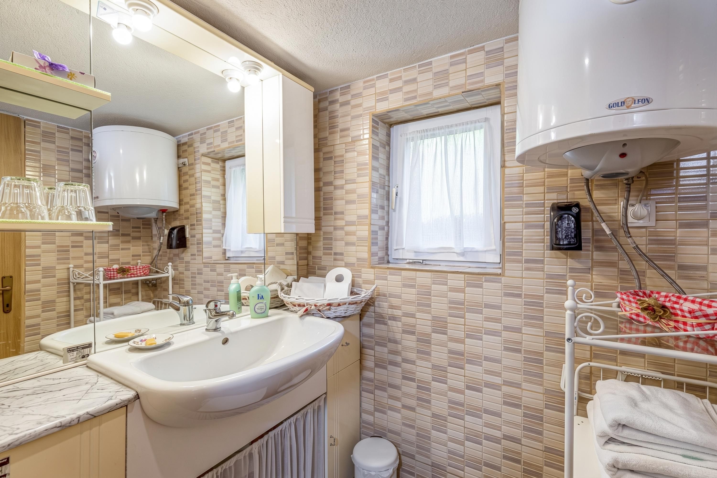 Un baño con lavamanos, espejo, toallero y ventana.