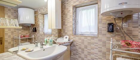 Un baño con lavamanos, espejo, toallero y ventana.