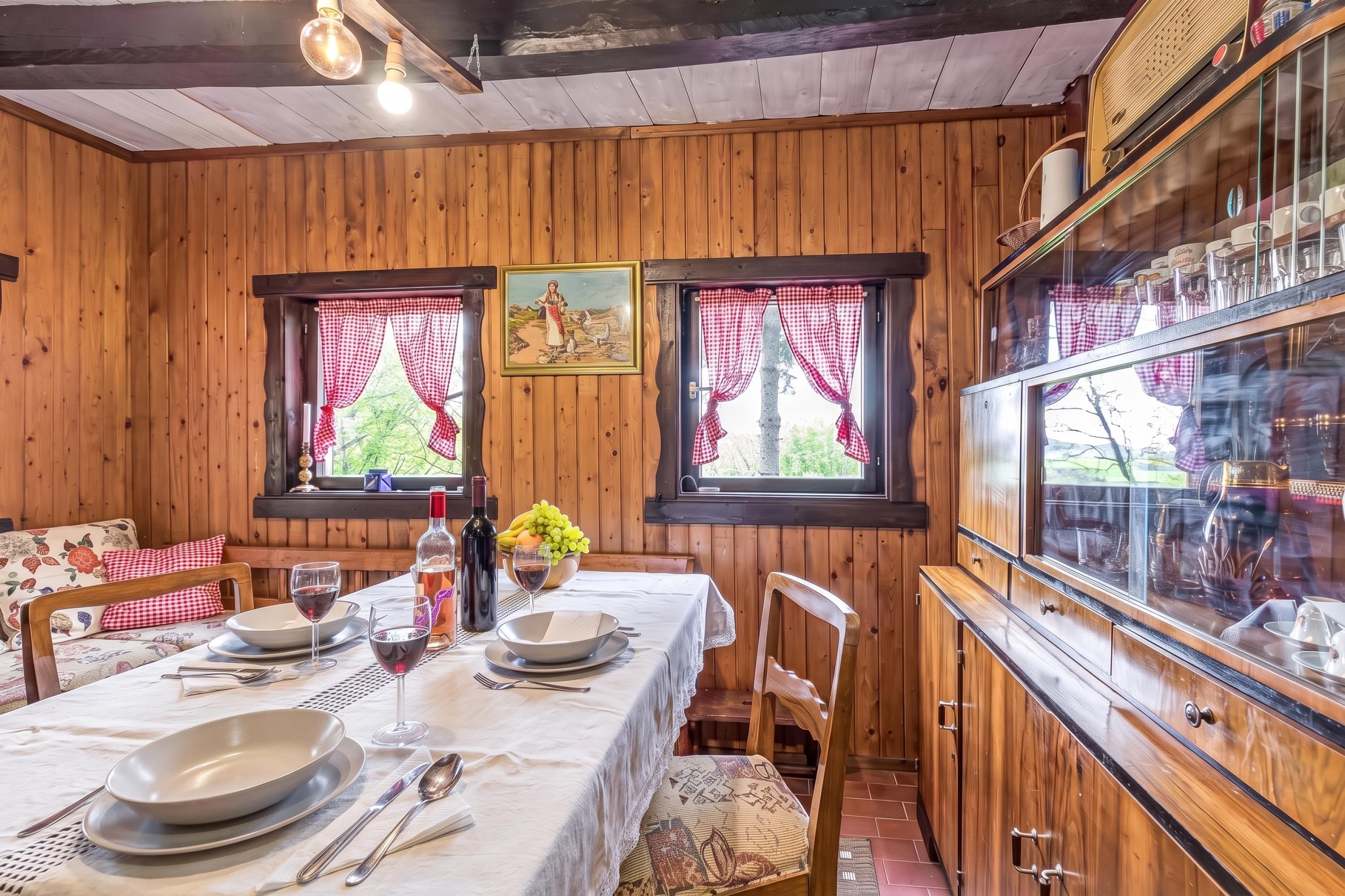 Ein Holzinterieur mit einem für zwei Personen gedecktem Esstisch, einer Weinflasche und einer Obstschale.