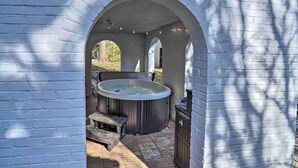 An outdoor hot tub area with a wooden bench and a wooden cabinet, enclosed by white brick walls with arches. - Historic Warrenton Home w/ Patio & Hot Tub! (Warrenton)