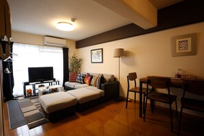 A living room with a sofa, ottoman, TV, and a dining area with chairs and a table.