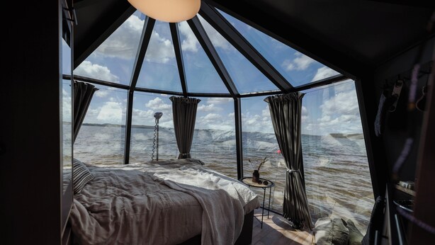 A cozy, modern room with a large bed, a small table, and a view of the ocean. - Yggdrasil Igloo Water Huts (Årjäng)