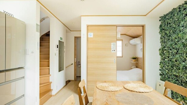 A modern hotel room with a wooden dining table, chairs, and a green leafy wall. - Private lodging in WEST TOKYO(SHINJUKU, TACHIKAWA, SANRIO, GHIBLI, MT. TAKAOetc) (Kokubunji)