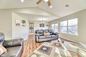 A spacious living room with a leather sofa, a patterned rug, and a large window providing natural light. - Fayetteville Home w/ Hot Tub ~ 3 Mi to U of A! (Fayetteville)