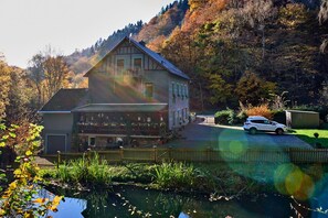 Ein traditionelles Chalet mit Balkon, einem geparkten Auto davor und einem Teich im Vordergrund.