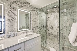 Ein modernes Badezimmer mit Marmorwänden, einer in Glas abgeschlossenen Dusche und einem Waschtisch mit Spiegel.