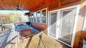 A wooden deck with a table and chairs, a large sliding door, and a view of trees in the background. - Luxury Lodge on 125 acres on Hocking Hills Farm (Logan)